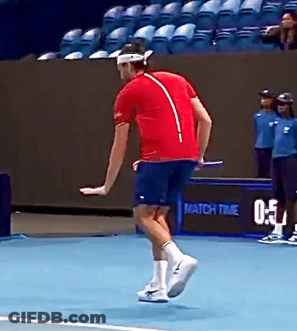 A Man In A Red Shirt And Blue Shorts Is Jumping On A Tennis Court . GIF