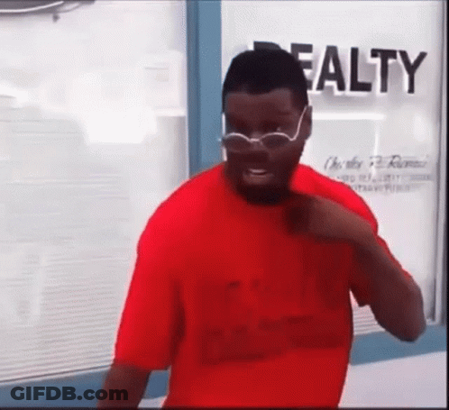 A Man In A Red Shirt And Glasses Is Standing In Front Of A Window . GIF