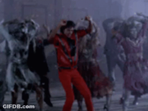 A Man In A Red Shirt And Red Pants Is Dancing In Front Of A Crowd Of Zombies . GIF