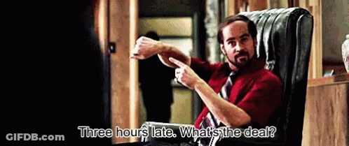 A Man In A Red Shirt And Tie Is Sitting In A Chair And Says Three Hours Late What 'S The Deal GIF