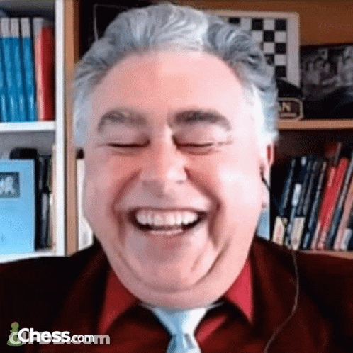A Man In A Red Shirt And Tie Is Smiling In Front Of A Bookshelf With Chess.com Written On The Bottom GIF