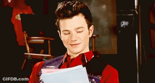 A Man In A Red Shirt And Vest Is Holding A Piece Of Paper And Smiling . GIF