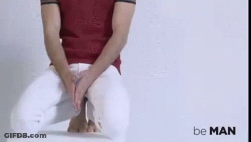 A Man In A Red Shirt And White Pants Is Sitting On A Chair With His Hands On His Lap . GIF