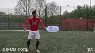 A Man In A Red Shirt And White Shorts Is Holding A Head & Shoulders Sign On A Soccer Field . GIF