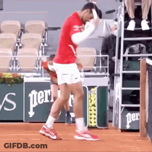 A Man In A Red Shirt And White Shorts Is Standing On A Tennis Court Holding A Tennis Racket . GIF