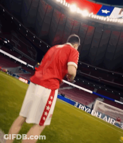 A Man In A Red Shirt And White Shorts Stands On A Soccer Field With An Ad For Riyadh Air Behind Him GIF