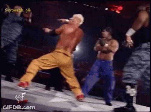 A Man In A Red Shirt And Yellow Pants Is Dancing On A Stage With Wrestlers In The Background GIF