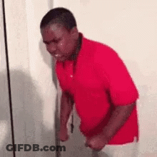 A Man In A Red Shirt Is Crying While Standing Next To A Door . GIF