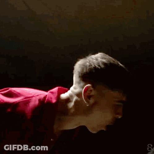 A Man In A Red Shirt Is Dancing In A Dark Room GIF