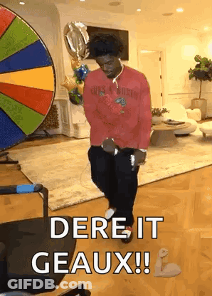 A Man In A Red Shirt Is Dancing In A Living Room In Front Of A Colorful Wheel . GIF