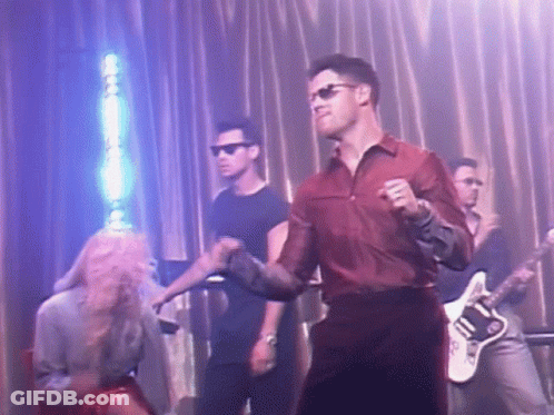 A Man In A Red Shirt Is Dancing On A Stage With A Guitar Player . GIF