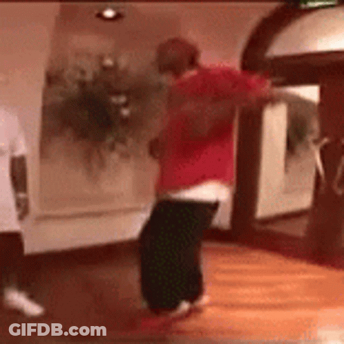 A Man In A Red Shirt Is Dancing On A Wooden Floor . GIF