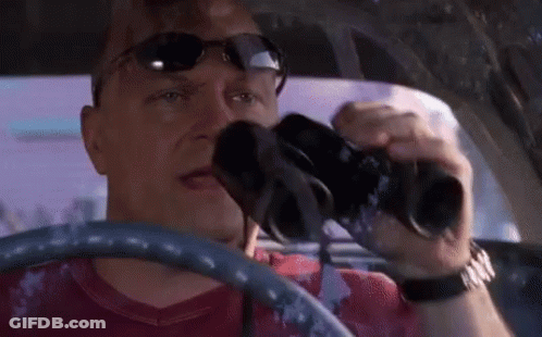 A Man In A Red Shirt Is Driving A Car And Looking Through Binoculars GIF
