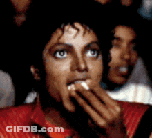 A Man In A Red Shirt Is Eating Something With His Hands GIF