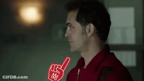 A Man In A Red Shirt Is Holding A Foam Finger In His Right Hand . GIF