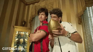 A Man In A Red Shirt Is Holding A Football Next To Another Man In A White Shirt GIF