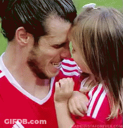 A Man In A Red Shirt Is Holding A Little Girl In His Arms And Kissing Her On The Forehead . GIF