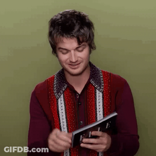 A Man In A Red Shirt Is Holding A Magazine In His Hands . GIF