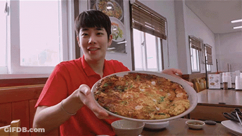 A Man In A Red Shirt Is Holding A Plate Of Food In His Hands GIF