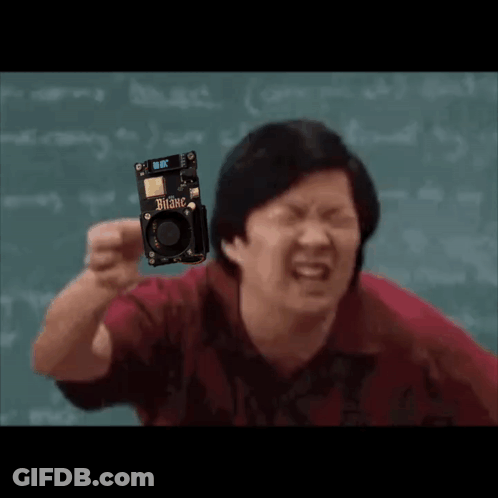 A Man In A Red Shirt Is Holding A Small Electronic Device . GIF