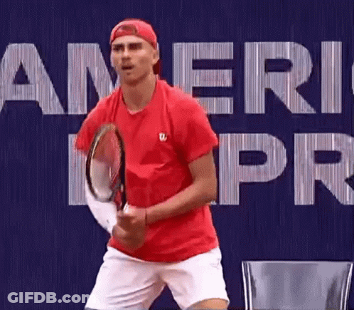 A Man In A Red Shirt Is Holding A Tennis Racket In Front Of A Blue Background . GIF
