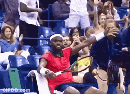 A Man In A Red Shirt Is Holding A Tennis Racquet In Front Of A Crowd GIF