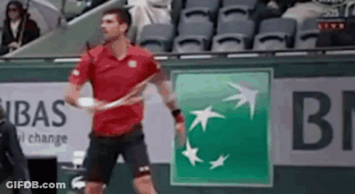 A Man In A Red Shirt Is Holding A Tennis Racquet In Front Of An Bnp Logo GIF