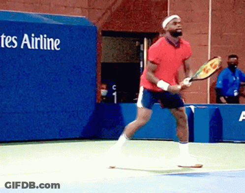 A Man In A Red Shirt Is Holding A Tennis Racquet On A Tennis Court In Front Of A Tes Airline Sign GIF