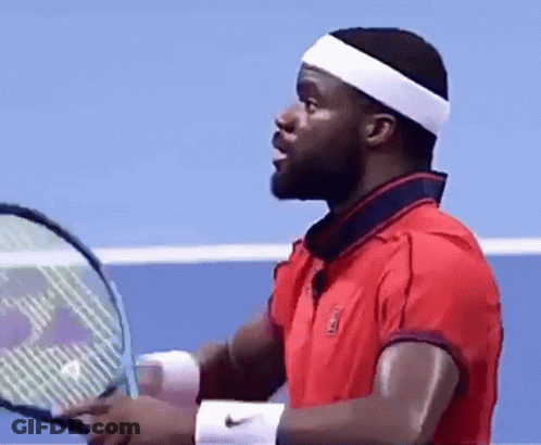 A Man In A Red Shirt Is Holding A Tennis Racquet On A Tennis Court . GIF