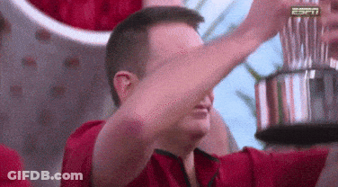 A Man In A Red Shirt Is Holding A Trophy And Covering His Face With His Hand . GIF