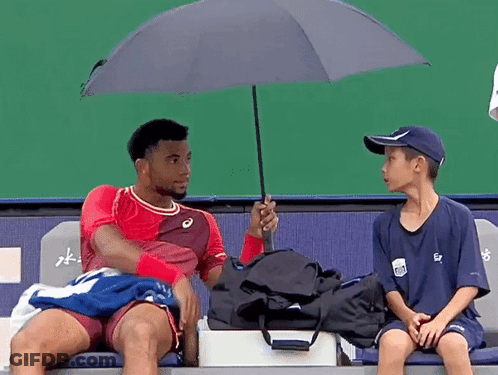 A Man In A Red Shirt Is Holding An Umbrella Over Another Man In A Blue Shirt GIF