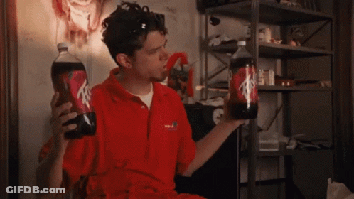 A Man In A Red Shirt Is Holding Two Bottles Of Soda One Of Which Has The Letter A On It GIF