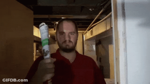 A Man In A Red Shirt Is Holding Up A Bottle Of Aerosol Spray GIF