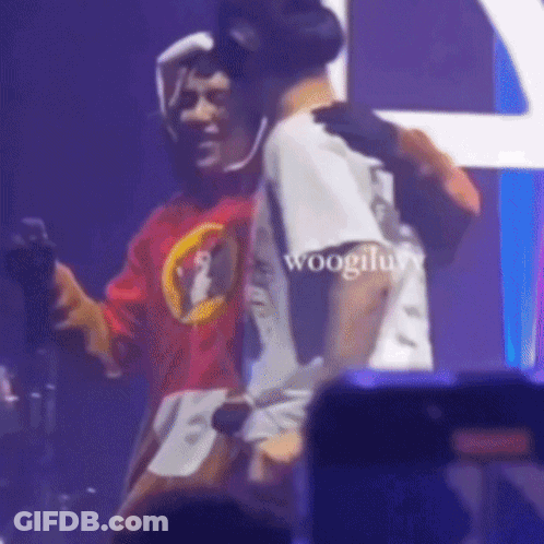 A Man In A Red Shirt Is Hugging Another Man In A White Shirt On Stage . GIF