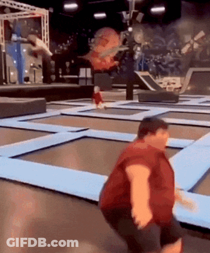 A Man In A Red Shirt Is Jumping On A Trampoline With A Child In The Background . GIF