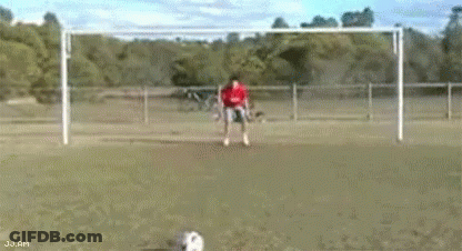 A Man In A Red Shirt Is Kicking A Soccer Ball Into A Soccer Goal . GIF