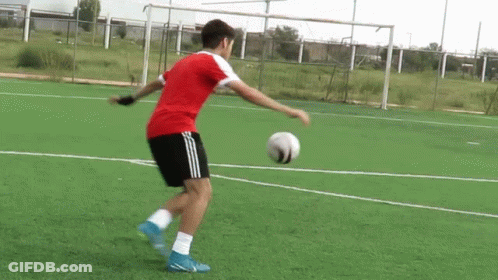 A Man In A Red Shirt Is Kicking A Soccer Ball On A Field . GIF