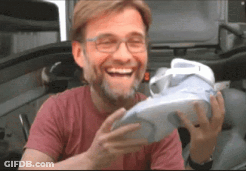 A Man In A Red Shirt Is Laughing While Holding A White Shoe GIF