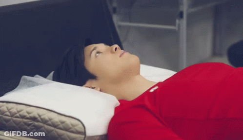 A Man In A Red Shirt Is Laying On A Bed With A Pillow And Looking Up . GIF