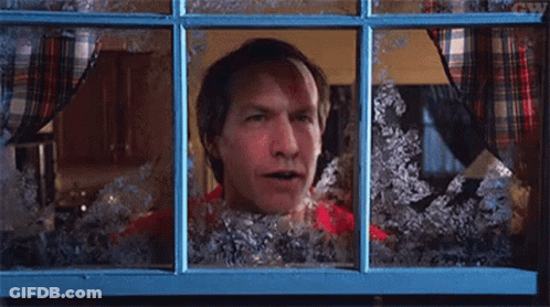 A Man In A Red Shirt Is Looking Out Of A Window Covered In Snow . GIF