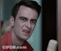 A Man In A Red Shirt Is Making A Funny Face While Leaning Against A Door . GIF