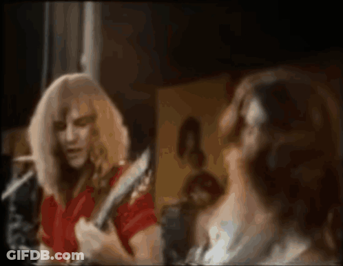 A Man In A Red Shirt Is Playing A Guitar In Front Of A Mirror While A Woman Looks On . GIF