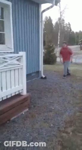 A Man In A Red Shirt Is Running In Front Of A Blue Building GIF