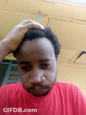 A Man In A Red Shirt Is Scratching His Head With His Hand GIF