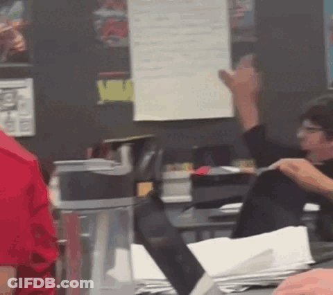 A Man In A Red Shirt Is Sitting At A Desk With A Laptop GIF