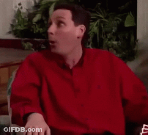 A Man In A Red Shirt Is Sitting In A Chair And Making A Funny Face . GIF
