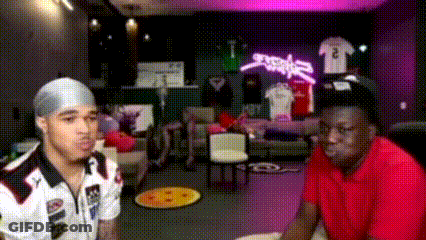 A Man In A Red Shirt Is Sitting Next To Another Man In A White Shirt GIF