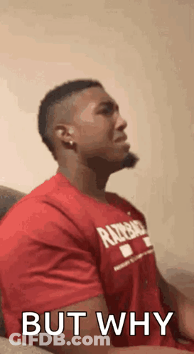 A Man In A Red Shirt Is Sitting On A Couch And Making A Face . GIF