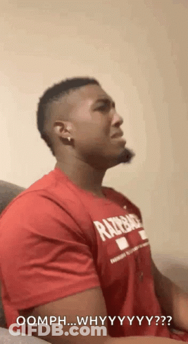 A Man In A Red Shirt Is Sitting On A Couch And Making A Funny Face . GIF