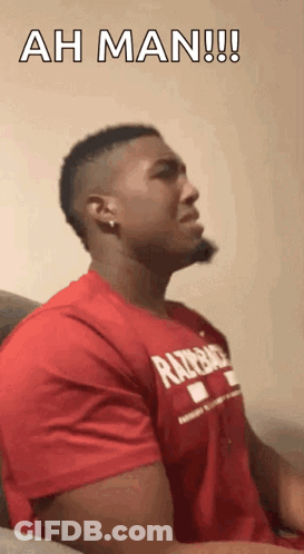A Man In A Red Shirt Is Sitting On A Couch And Says Ah Man !! GIF